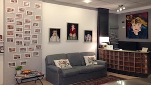 A reception area with a grey sofa, a coffee table, and a wall decorated with framed pictures and a large painting. - Hotel Genziana (Genoa)