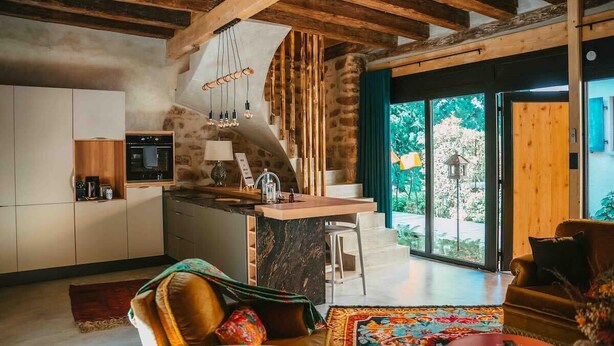 Une cuisine moderne dotée d’un îlot en marbre, de poutres en bois et offrant une vue sur la verdure environnante.