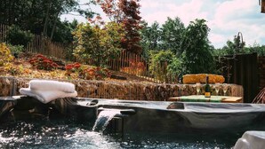 Un bain à remous agrémenté d’une cascade, entouré d’une clôture en bois et d’un jardin aux couleurs automnales.