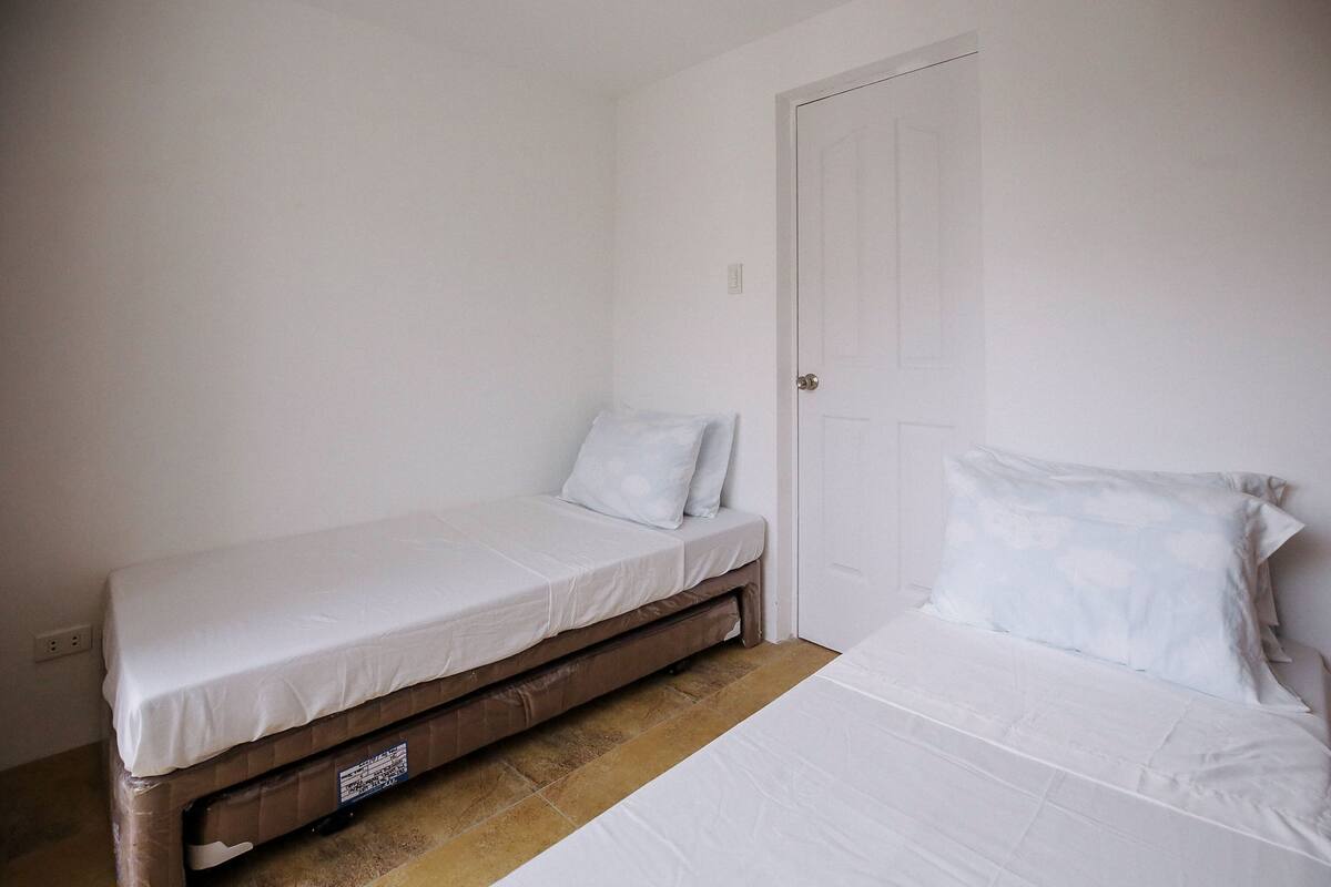 A small, single-bed room with a wooden bed frame, white bedding, and a closed door.