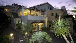 Uma casa de dois andares com varanda, alpendre e jardim com diversas plantas.