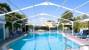 Piscina com toldo branco, rodeada por cadeiras de descanso azuis.