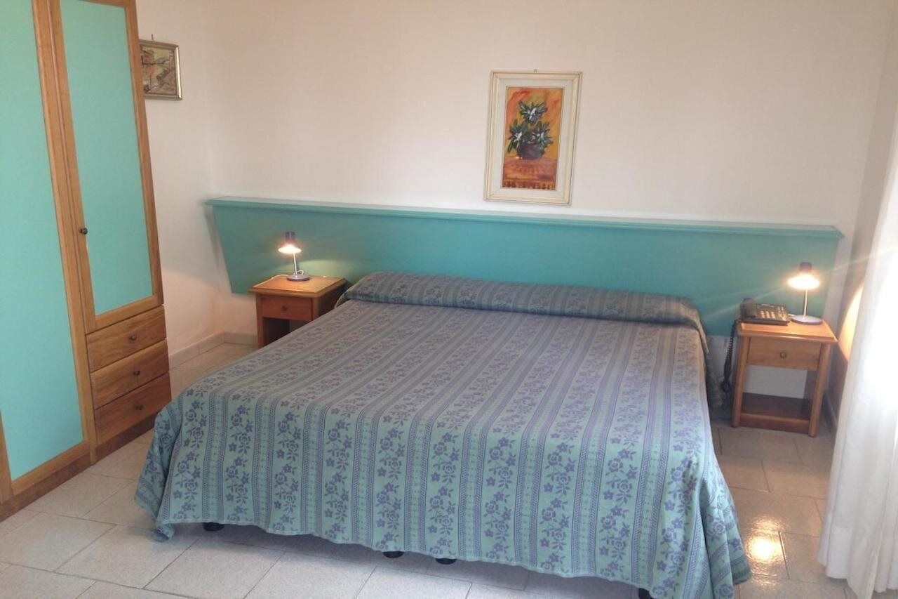 Un dormitorio con una cama, dos mesitas de noche, un aparador y un armario de madera, además de un cuadro en la pared.