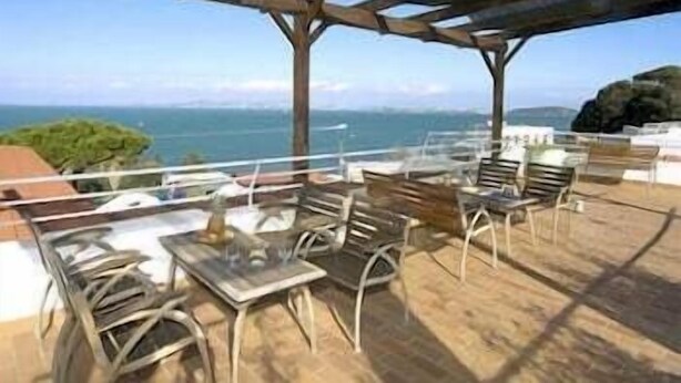 Terraço ao ar livre com mesas e cadeiras, com vista para um corpo de água e colinas.