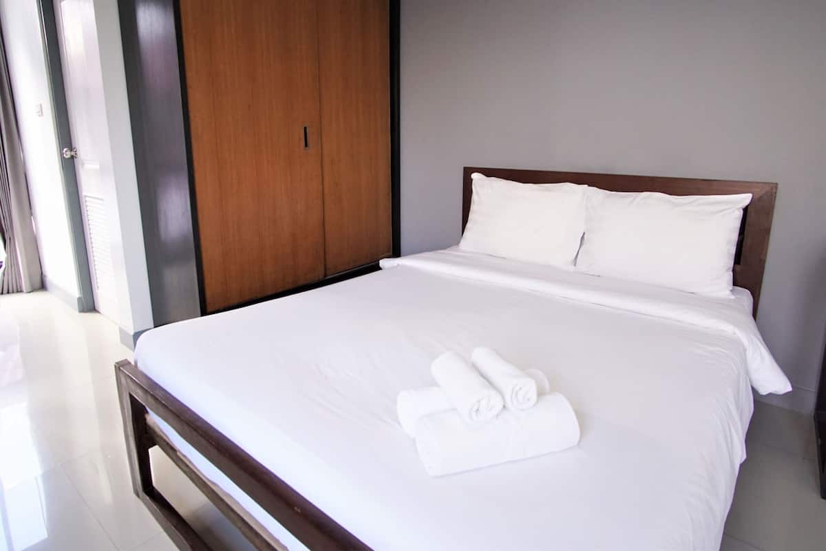 A hotel room with a large bed, white linens, a wooden headboard, and a wardrobe.