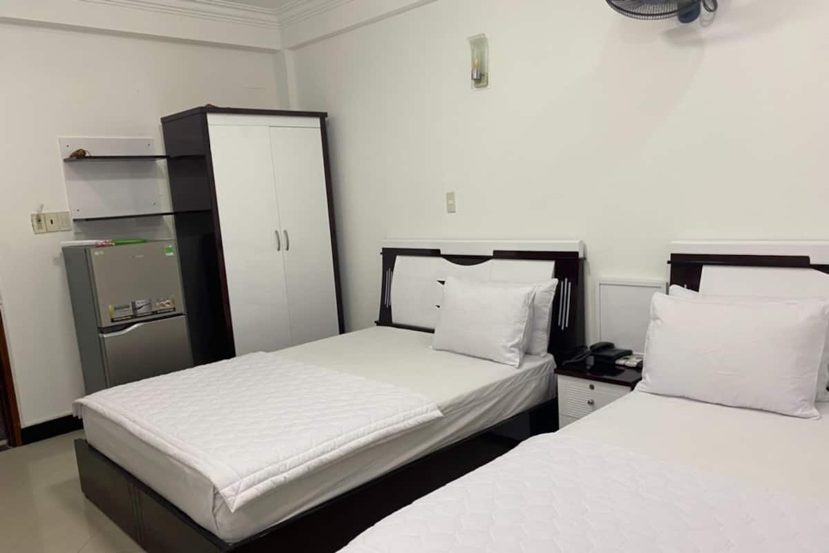 A hotel room with two beds, a wardrobe, a refrigerator, and a bedside table with a phone.