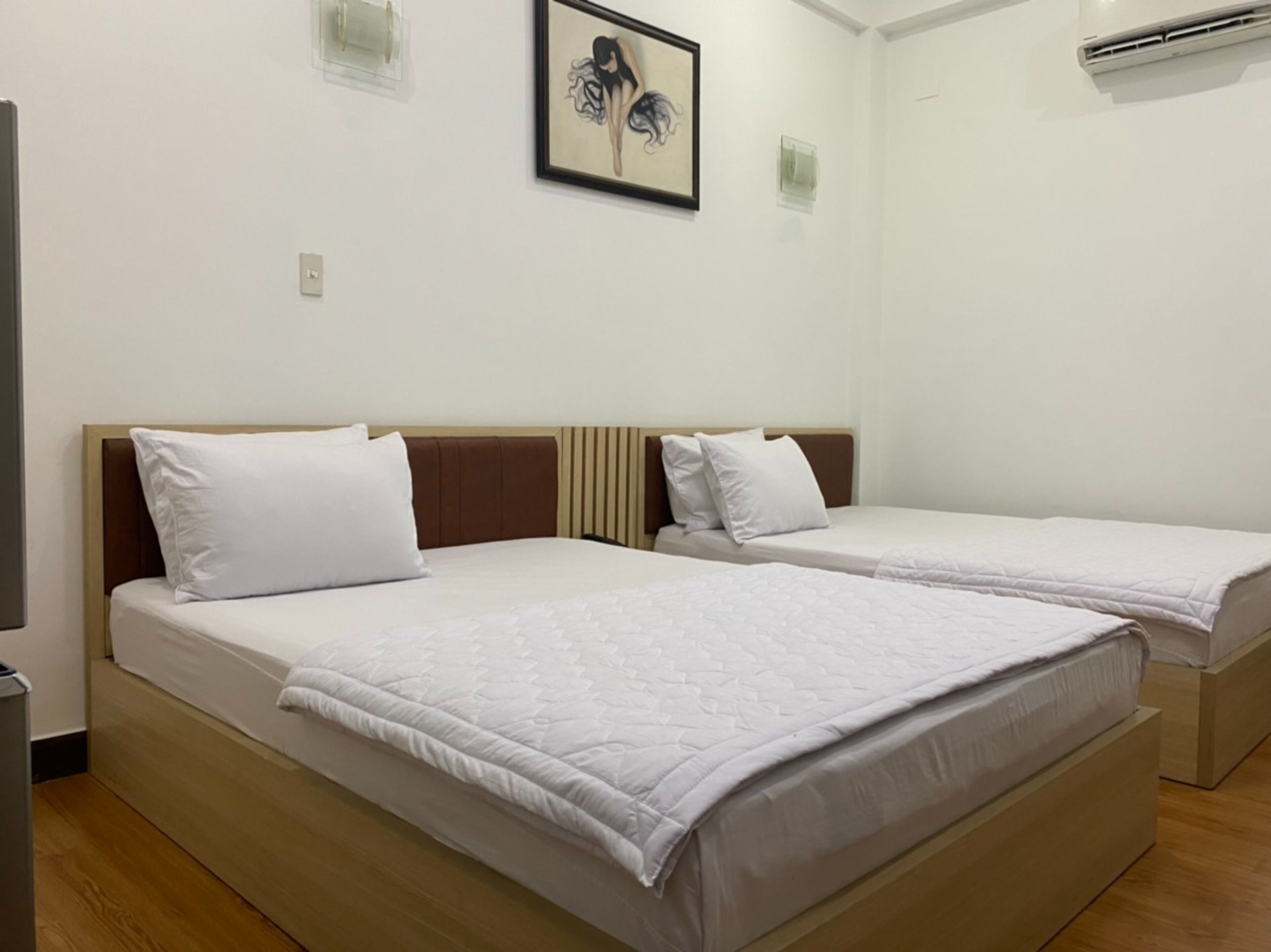 Habitación de hotel con dos camas individuales, suelo de madera, pared blanca y una obra de arte enmarcada sobre las camas.