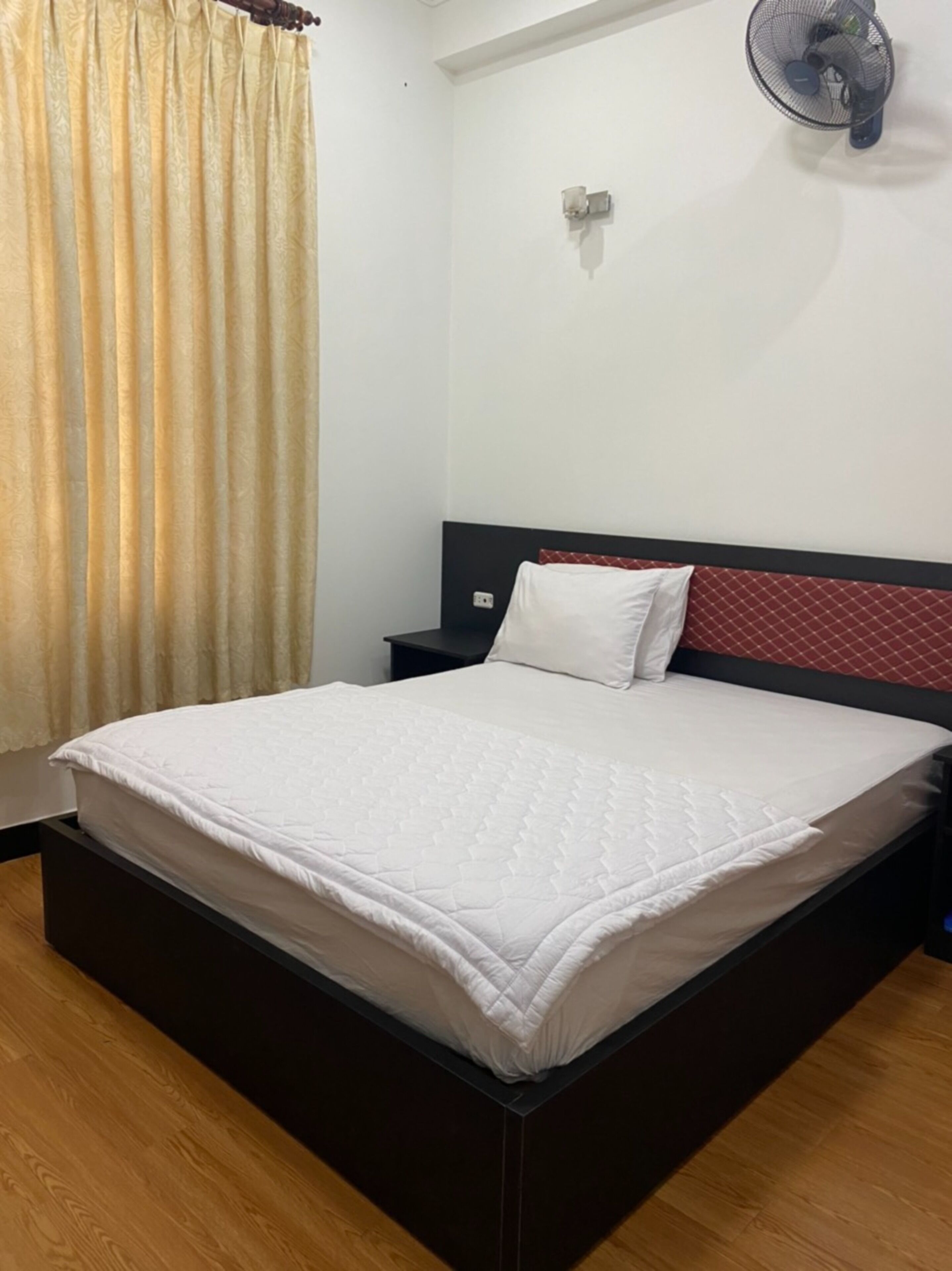 A neatly made bed with a white quilt, a red headboard, and a small bedside table with a lamp.