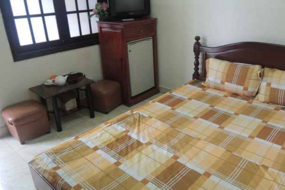 A bedroom with a bed, a wooden headboard, a small table with a chair, and a television on a cabinet.