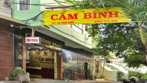 A multi-story building with a green facade and a yellow sign reading "CÂM BINH".