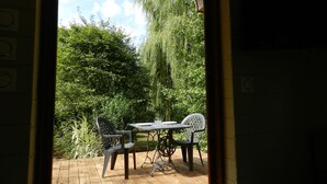 Un espace extérieur aménagé en terrasse, avec une table et des chaises, entouré d’une végétation luxuriante et d’un saule pleureur.
