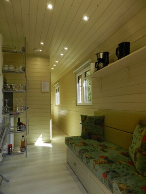 A cozy room with a sofa, shelves with glassware, a window, and a ceiling with recessed lighting.