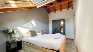 A bedroom with a skylight, a bed with white bedding, a nightstand with a lamp, and a dark wardrobe.