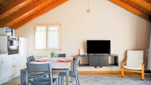 A dining area with a table set for two, a television on a stand, and a kitchen with appliances.