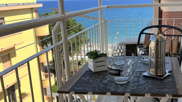 A balcony with a table set for breakfast, overlooking a coastal view.