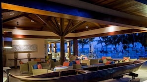 An indoor lounge area with a boat-shaped seating arrangement, wooden beams, and a view of palm trees. - Jatiuca Hotel and Resort (Maceió)