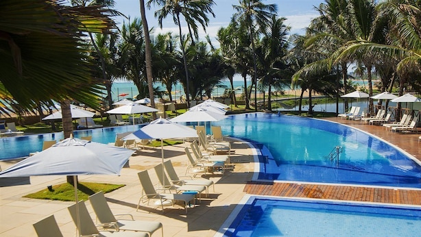 A swimming pool with lounge chairs and umbrellas, surrounded by palm trees and a view of the beach. - Jatiuca Hotel and Resort (Maceió)