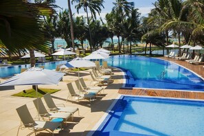 A swimming pool with lounge chairs and umbrellas, surrounded by palm trees and a view of the beach. - Jatiuca Hotel and Resort (Maceió)