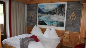 Una cama de madera con ropa de cama blanca, una toalla roja y un cuadro de un paisaje montañoso en la pared.