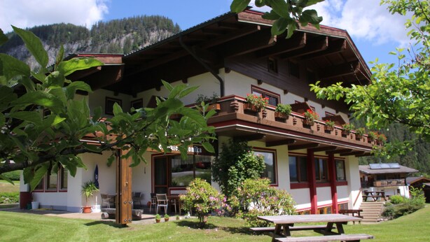 Un chalet con balcón, jardín y montañas al fondo.
