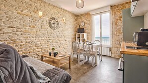 A cozy living room with a stone wall, a wooden table, and a sofa. - Charmant T2 Vue Mer Décoration Soignée (Saint-Aubin-sur-Mer)