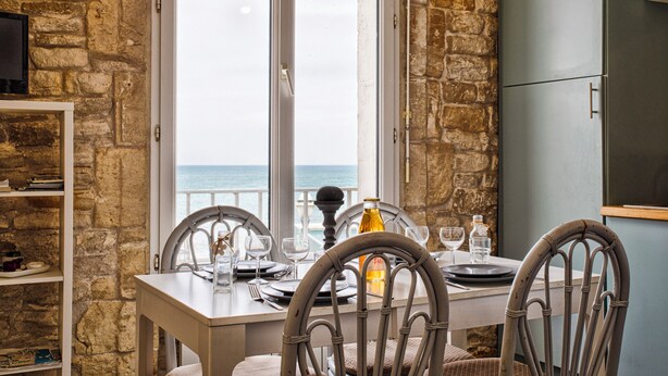 A dining table set for four with chairs, a view of the sea, and a stone wall. - Charmant T2 Vue Mer Décoration Soignée (Saint-Aubin-sur-Mer)