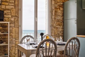 A dining table set for four with chairs, a view of the sea, and a stone wall.
