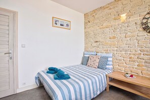 A bedroom with a stone wall, a bed with striped bedding, a bedside table with a plate, and a framed picture on the wall.