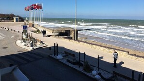 A coastal promenade with a clear view of the sea, a pedestrian path, and a flagpole. - Charmant T2 Vue Mer Décoration Soignée (Saint-Aubin-sur-Mer)