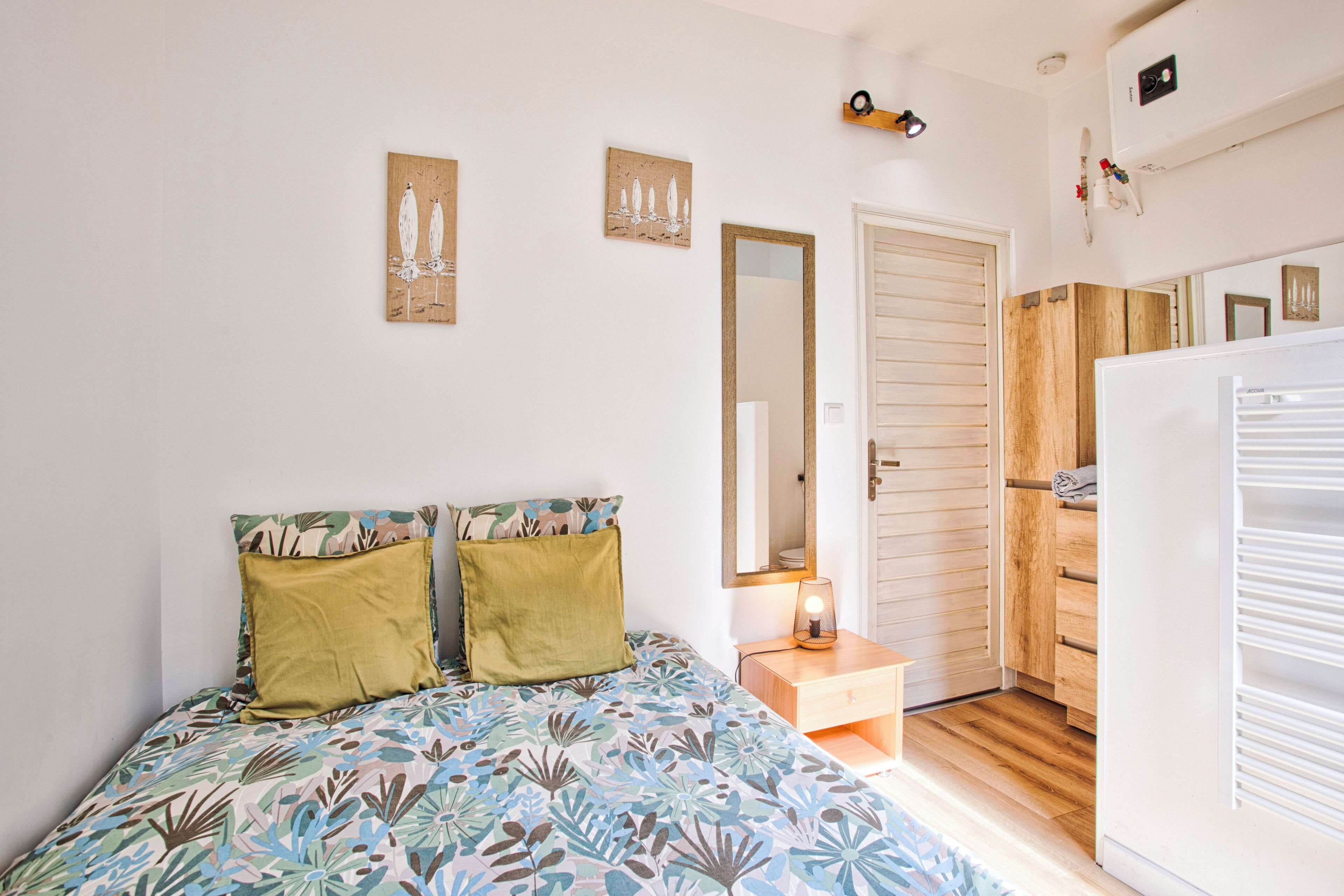 Une chambre à coucher comprenant un lit, une table de chevet, un miroir, une armoire et une porte.