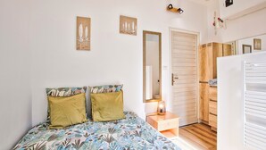 A bedroom with a bed, bedside table, mirror, wardrobe, and a door. - Charmant T2 Vue Mer Décoration Soignée (Saint-Aubin-sur-Mer)