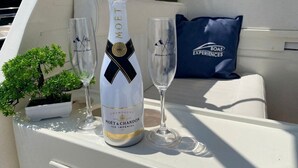 A bottle of Moët & Chandon champagne and two glasses on a boat deck, with a small potted plant and a blue pillow with the text "Boat Experiences". - Boating Oliday (Castellammare di Stabia)
