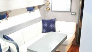 A compact living space with a white sofa, a small table, and a window. - Boating Oliday (Castellammare di Stabia)