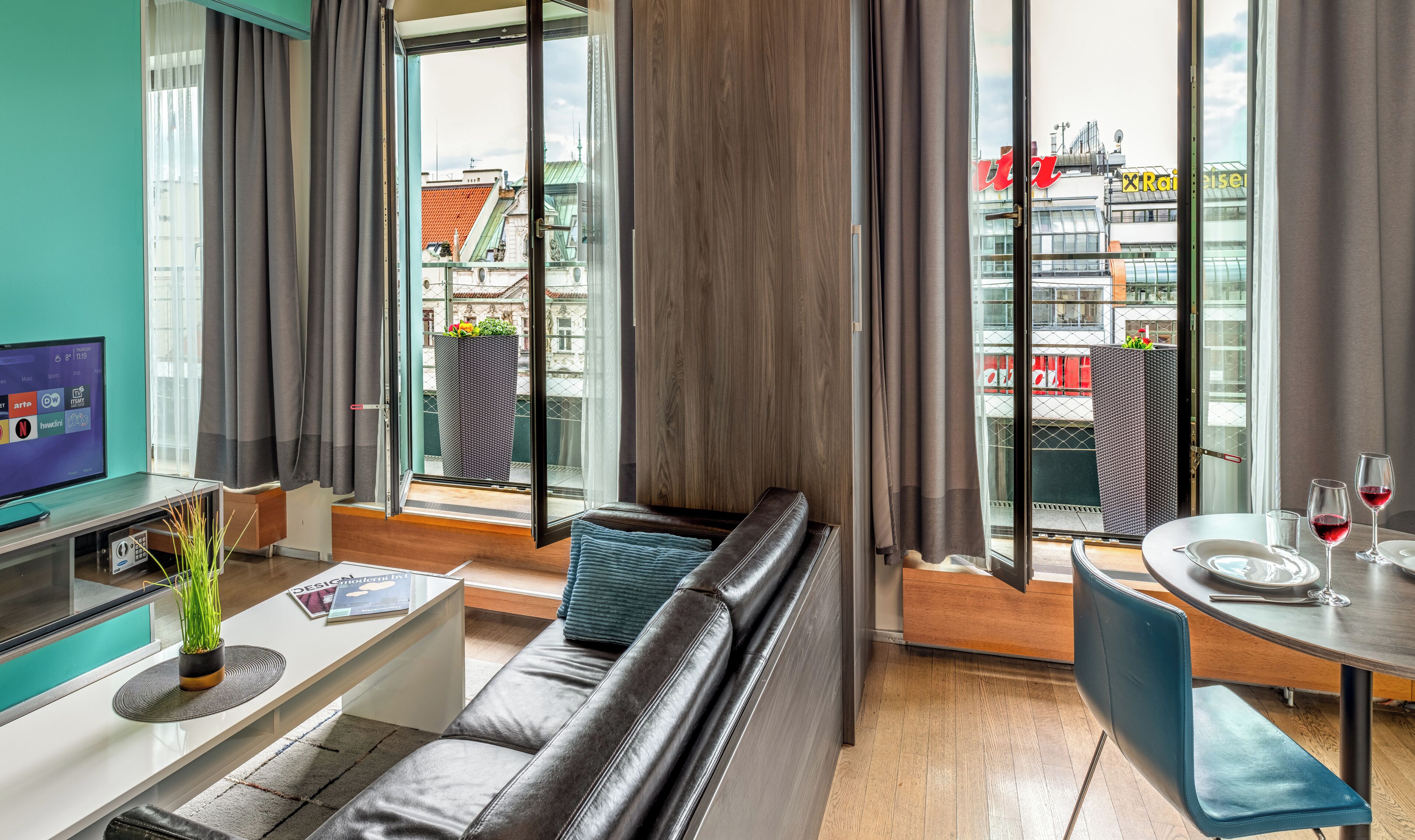 A modern living room with a sofa, a coffee table, a TV, and a balcony with a view of buildings.