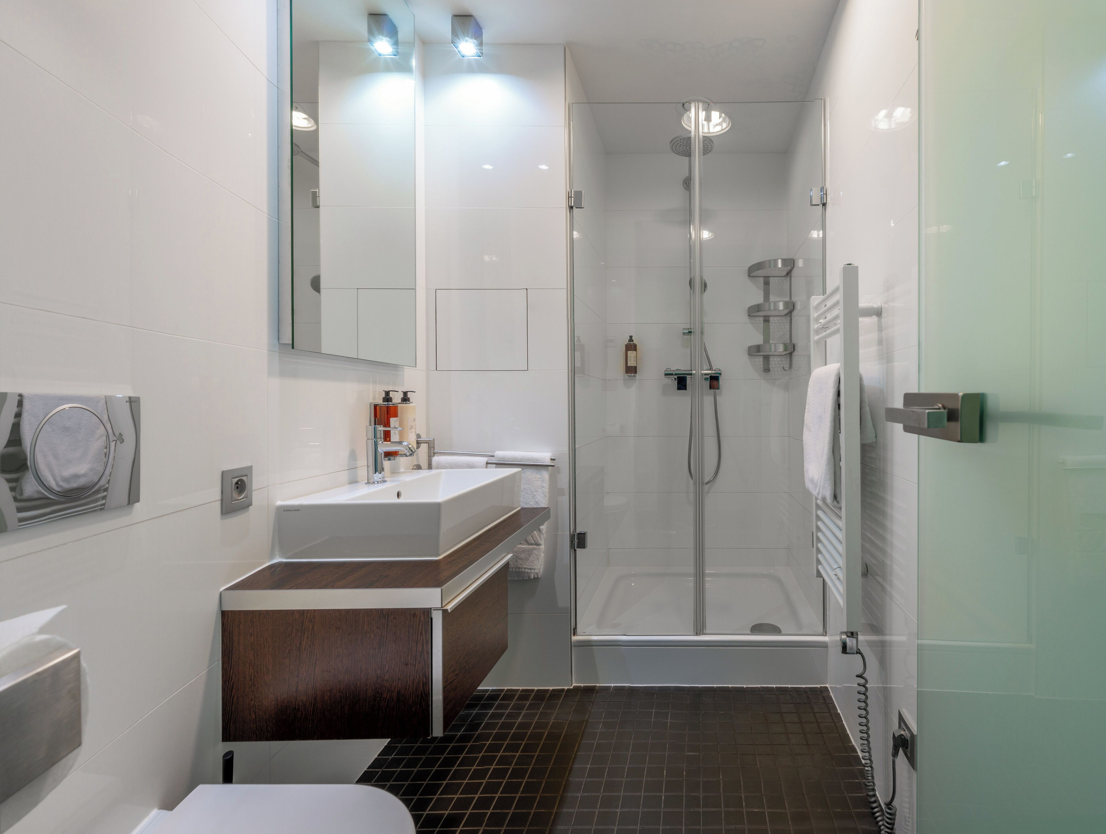 A modern bathroom with a glass-enclosed shower, a white sink with a wooden vanity, and a large mirror.