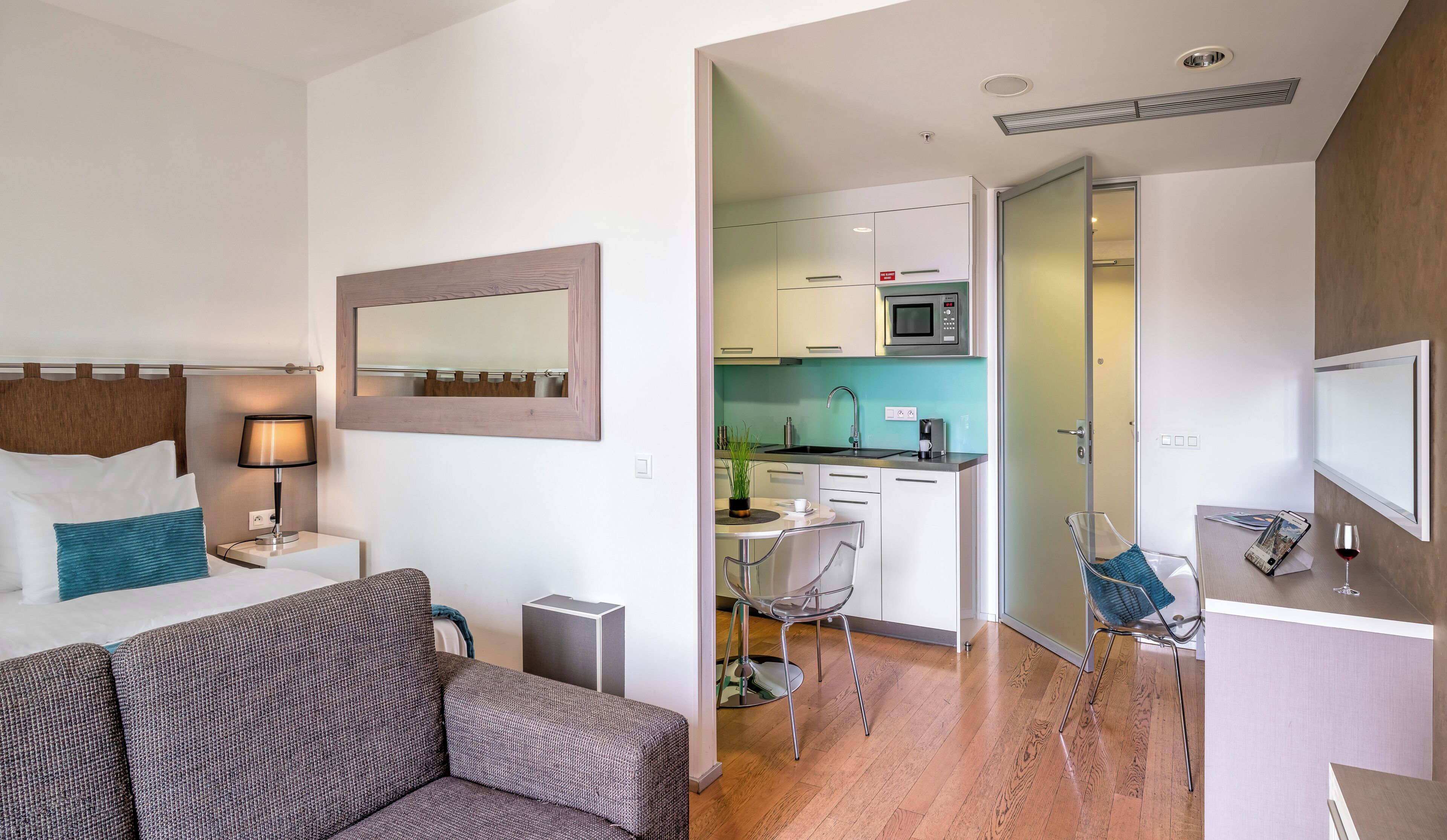 Una habitación de hotel moderna con una cama, mesita de noche, lámpara y vistas al área de la cocina contigua.