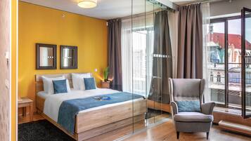 Una habitación de hotel moderna con una cama, una silla, una mesita y un ventanal grande con cortinas.