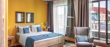 Een moderne hotelkamer met een bed, een stoel, een klein tafeltje en een groot raam met gordijnen.