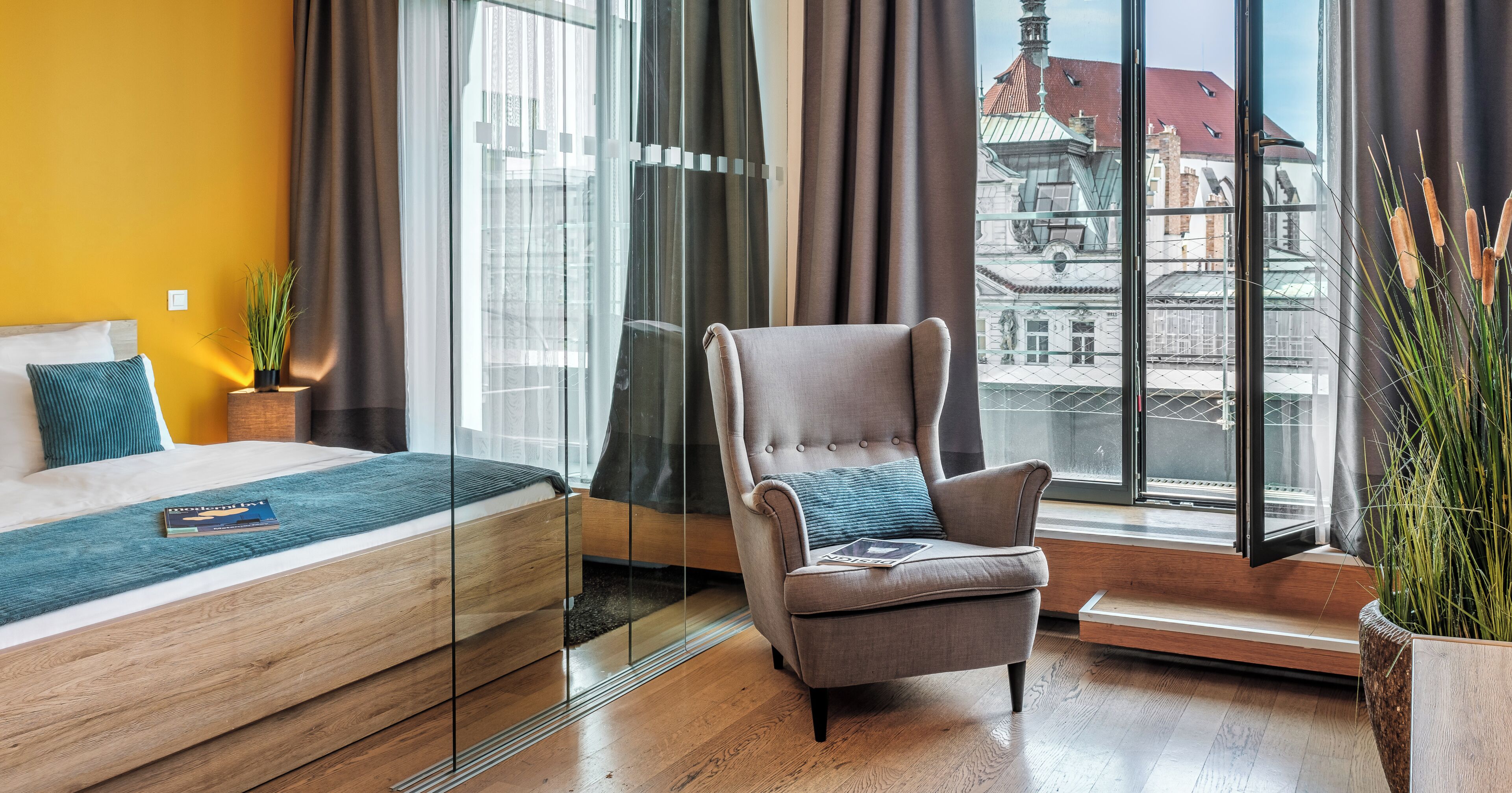 Una habitación de hotel moderna con una cama, una silla, un ventanal con vistas a la ciudad y una planta en maceta.
