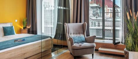 Una habitación de hotel moderna con una cama, una silla, un ventanal con vistas a la ciudad y una planta en maceta.