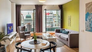 A modern living room with a sofa, chairs, a coffee table, and a TV. A large window offers a view of a cityscape and a building with a dome.