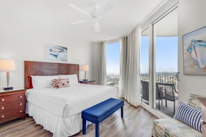 Habitación de hotel con una cama grande, una banca, un balcón con vistas y un ventilador de techo.