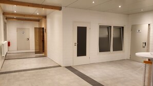 Ein modernes Badezimmer mit weißen Wänden, gefliestem Boden und Holzboden. Zwei Türen, eine zum Duschbereich und eine zur Toilette.