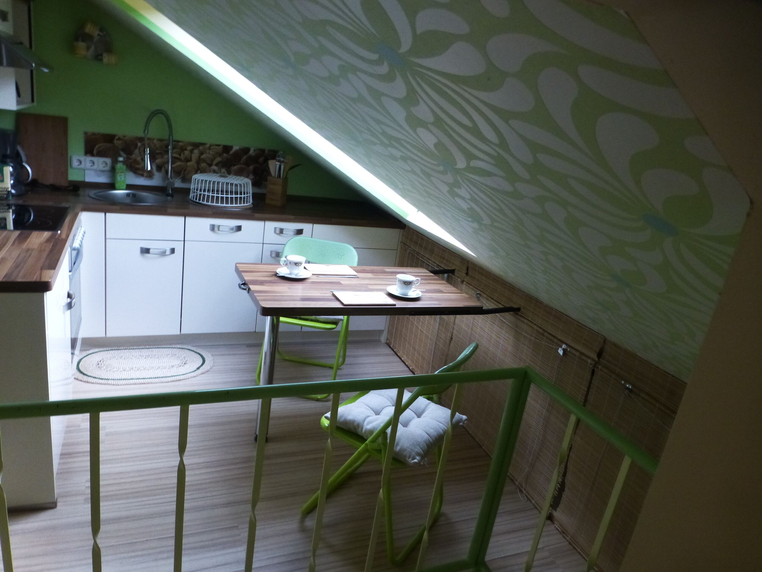 Una pequeña cocina americana con encimera de madera, un fregadero y una estufa. Hay una mesa con dos sillas y una ventana encima.