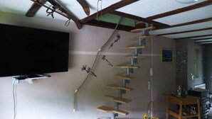 A staircase with wooden steps and a rope ladder, a flat-screen TV mounted on the wall, and a small table with a basket of sunflowers. - Castle view apartment 1 (Großlohra)