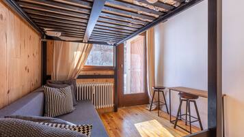 Une pièce chaleureuse avec un plafond en bois, un canapé agrémenté de coussins à motifs, une petite table et une fenêtre donnant sur l’extérieur.
