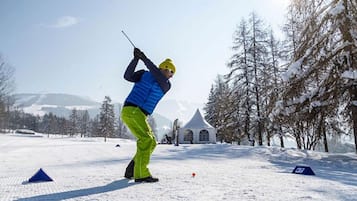 A person playing golf in a snowy outdoor setting with tents and trees in the background.