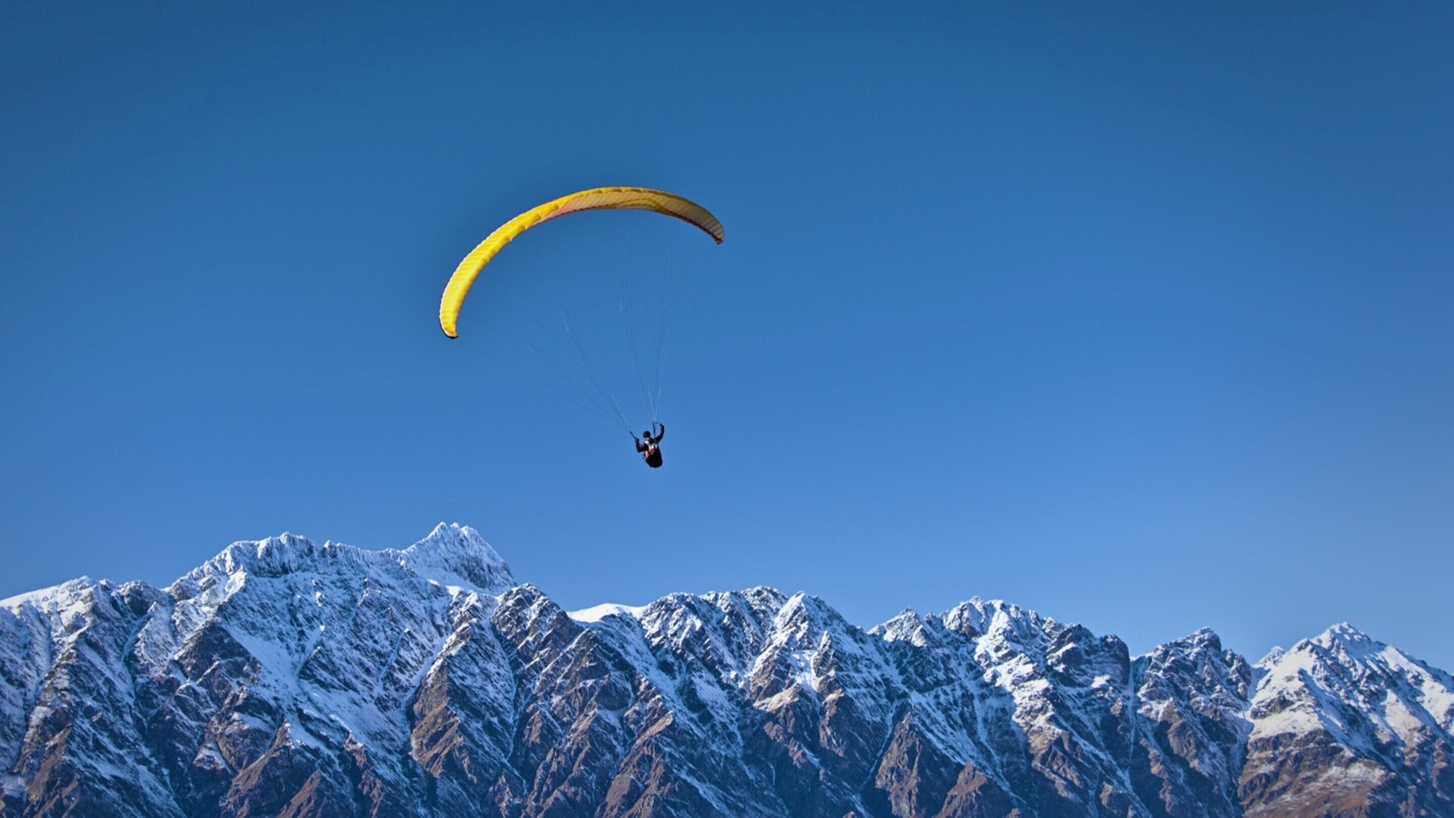 A person paragliding over snow-covered mountains.