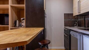 A compact kitchen with wooden cabinets, a stainless steel dishwasher, and a wooden countertop.