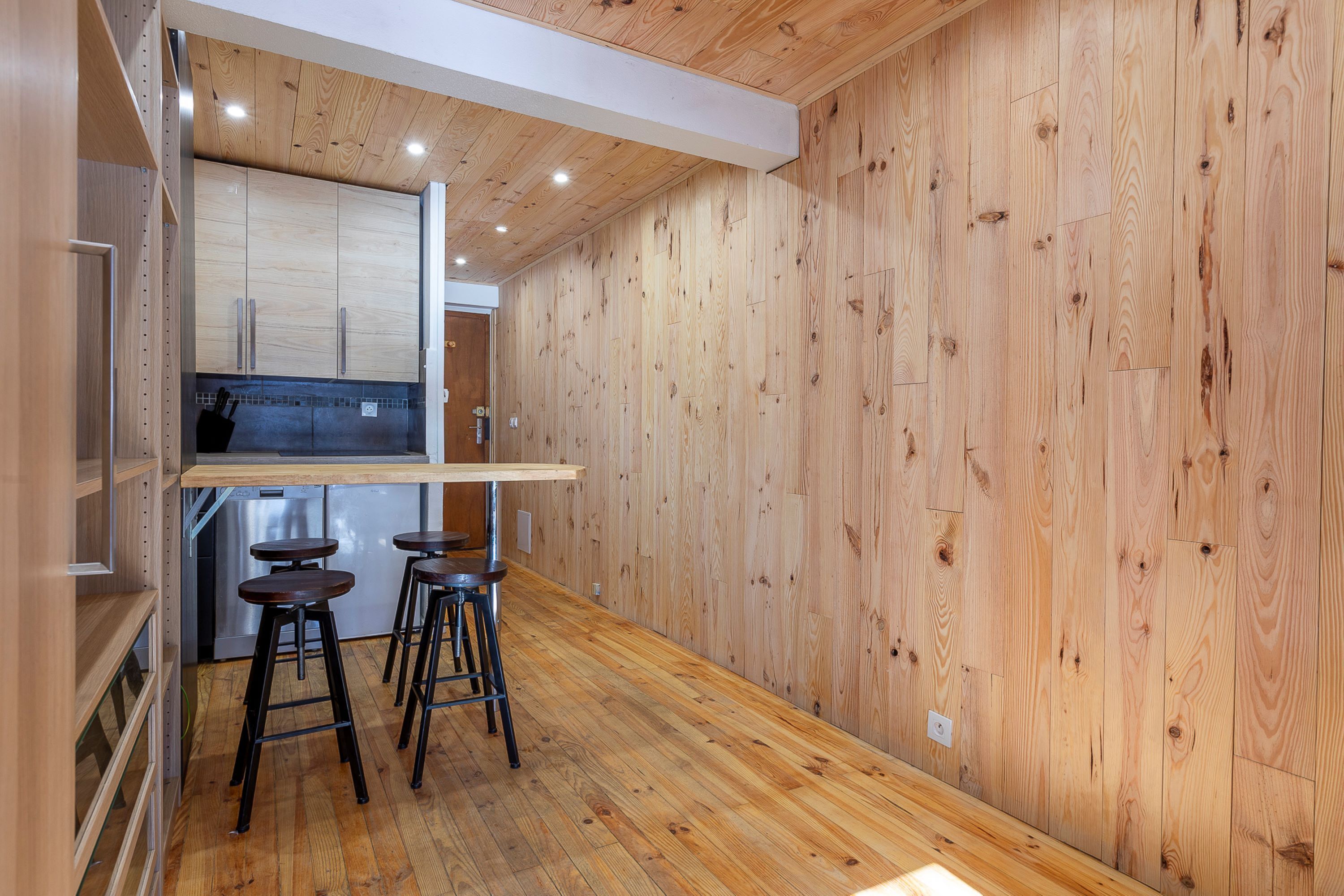 Una cocina compacta con paredes de madera, una barra integrada y tres taburetes.